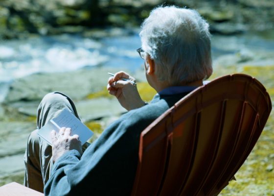 Clark Strand sitting by a stream writing haiku in a notebook.