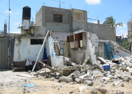 destroyed building in Palestine with woman wearing a khimar sitting on couch outside for story by an Israeli buddhist